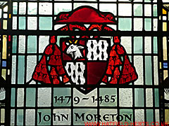 Stained glass coat of arms of Bishop John Moreton - quartered shield with diagonally opposite red and white quarters with a red bishops mitre helm and supporters